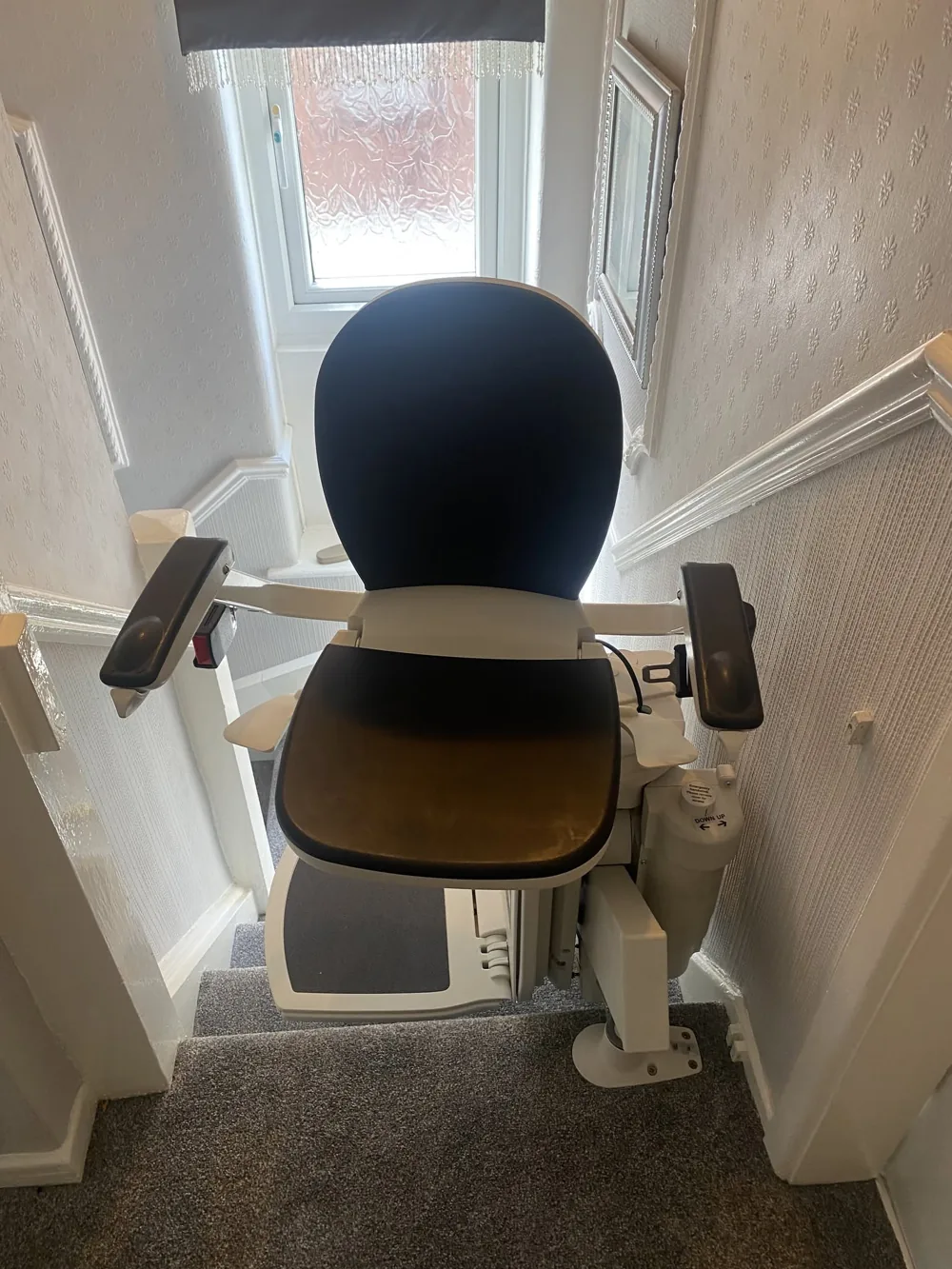 Reconditioned stairlift with dark upholstery parked at the top of a staircase in a Greater Manchester home